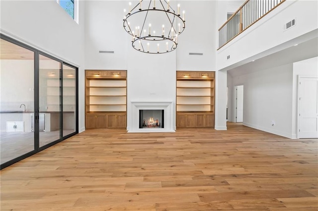 136 Linnette Ln, Mandeville, LA 70471 - unfurnished living room with a high ceiling, a chandelier, light wood-type flooring, baseboards, and a lit fireplace