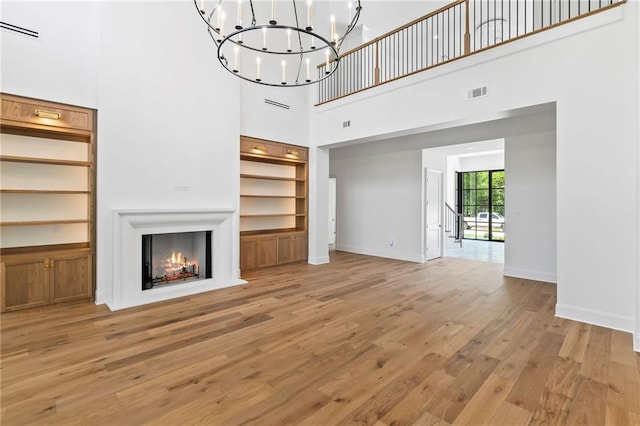 136 Linnette Ln, Mandeville, LA 70471 - unfurnished living room with built in features, light wood finished floors, a towering ceiling, a chandelier, and a warm lit fireplace