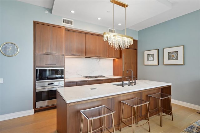 kitchen with appliances with stainless steel finishes, baseboards, a sink, a kitchen bar, and brown cabinetry