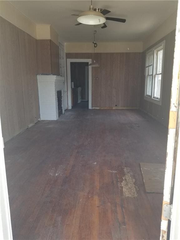 11921 Hesper Ave, Metairie, LA 70005 - unfurnished room with wooden walls, dark wood-style flooring, a brick fireplace, and a ceiling fan