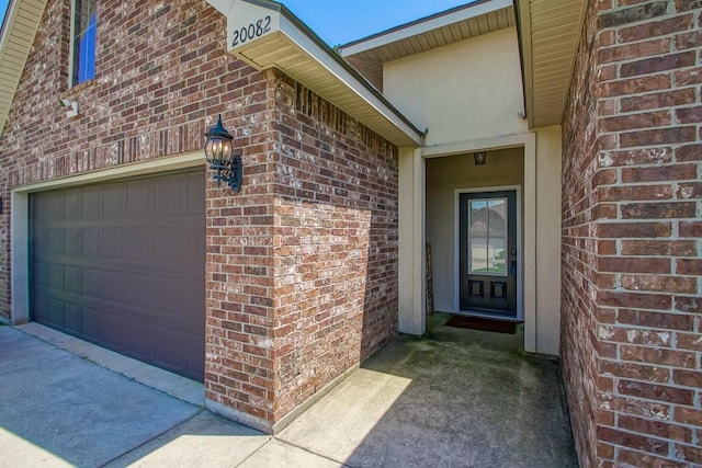 doorway to property featuring brick siding, an attached garage, and concrete driveway
