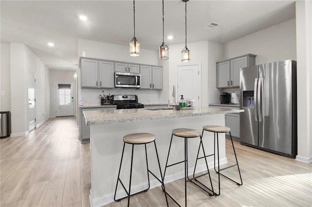 kitchen with appliances with stainless steel finishes, gray cabinets, light wood finished floors, a breakfast bar, and recessed lighting
