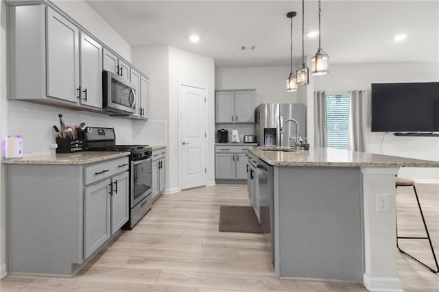 kitchen with stainless steel appliances, gray cabinetry, a sink, tasteful backsplash, and light wood-type flooring