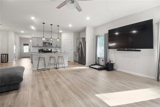 living area with ceiling fan, light wood-style floors, recessed lighting, healthy amount of natural light, and baseboards