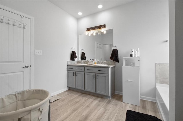full bathroom with wood finished floors, a tub to relax in, double vanity, baseboards, and recessed lighting