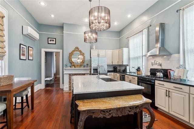 3451 Constance St, New Orleans, LA 70115 - kitchen featuring black range with gas stovetop, wall chimney range hood, a sink, stainless steel fridge, and a chandelier
