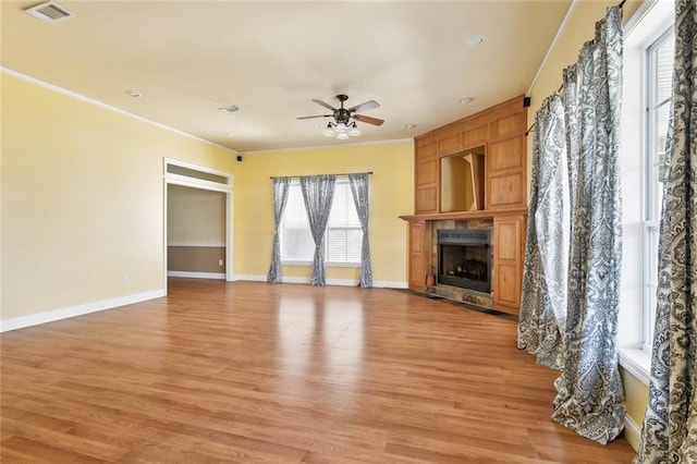 unfurnished living room with a ceiling fan, healthy amount of natural light, a fireplace, light wood finished floors, and crown molding
