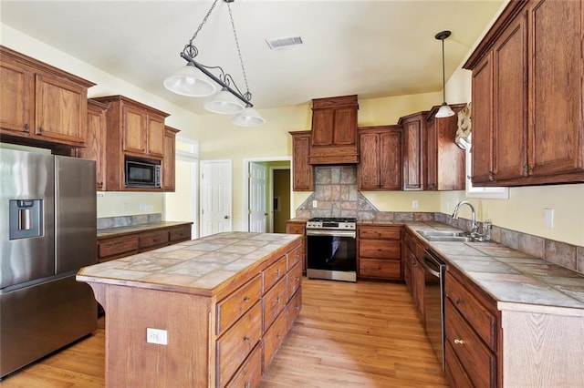 kitchen featuring appliances with stainless steel finishes, a sink, tile countertops, light wood-style flooring, and pendant lighting