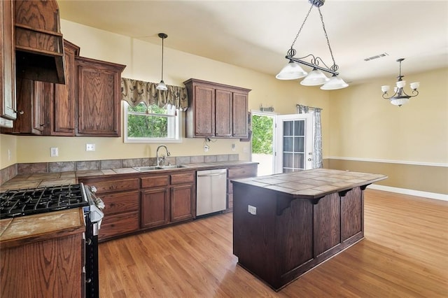 kitchen with appliances with stainless steel finishes, a sink, tile countertops, light wood-type flooring, and pendant lighting