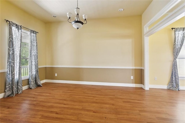 unfurnished room featuring wood finished floors, a chandelier, and baseboards