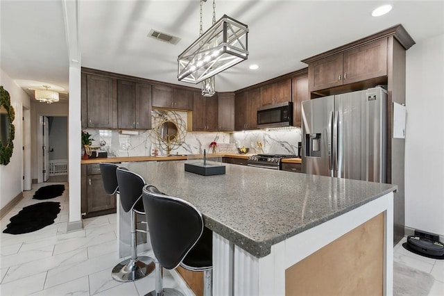 kitchen featuring stainless steel appliances, light marble finish floors, dark stone countertops, dark brown cabinets, and tasteful backsplash