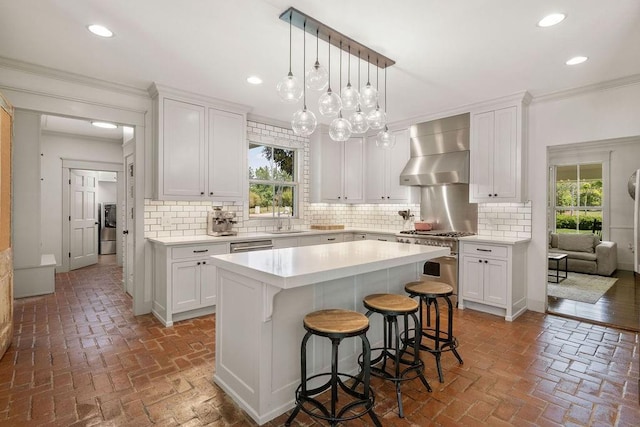 4 Riverdale Dr, Covington, LA 70433 - kitchen featuring wall chimney exhaust hood, stainless steel stove, brick flooring, crown molding, and white cabinets