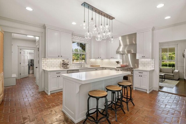 4 Riverdale Dr, Covington, LA 70433 - kitchen featuring high end stainless steel range oven, wall chimney exhaust hood, brick floors, ornamental molding, and white cabinets
