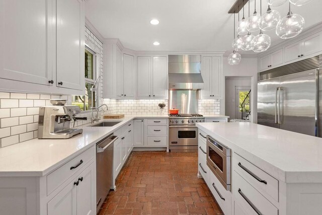 4 Riverdale Dr, Covington, LA 70433 - kitchen featuring built in appliances, wall chimney exhaust hood, brick flooring, white cabinets, and recessed lighting