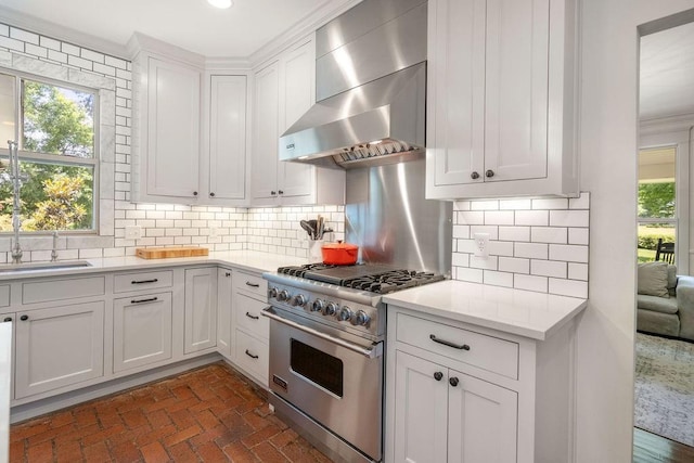 4 Riverdale Dr, Covington, LA 70433 - kitchen with high end stove, wall chimney range hood, light countertops, brick flooring, and white cabinets