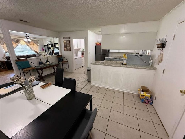 9425 Dancy Ave, Baton Rouge, LA 70814 - kitchen featuring freestanding refrigerator, light tile patterned flooring, a textured ceiling, light countertops, and white cabinetry