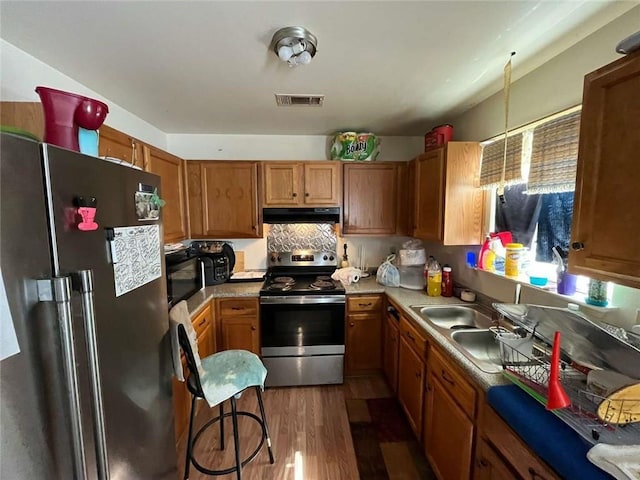 3319 N Dorgenois St, New Orleans, LA 70117 - kitchen featuring appliances with stainless steel finishes, brown cabinets, dark wood-style floors, under cabinet range hood, and light countertops