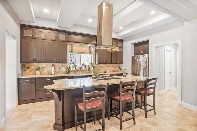 kitchen featuring appliances with stainless steel finishes, tasteful backsplash, dark brown cabinets, a kitchen island, and a breakfast bar
