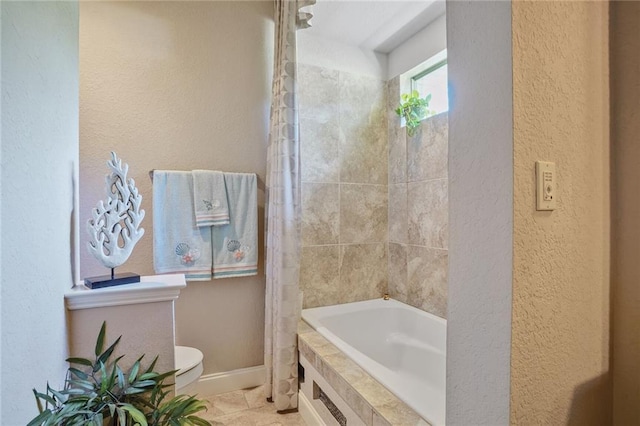 bathroom with toilet, baseboards, a textured wall, and tiled shower / bath
