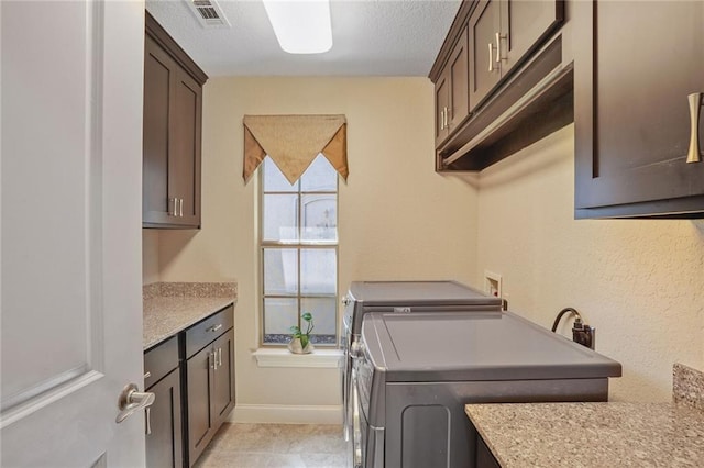 laundry area featuring cabinet space, separate washer and dryer, baseboards, a textured ceiling, and light tile patterned floors