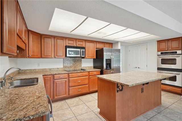 kitchen with stainless steel appliances, a sink, light tile patterned flooring, and brown cabinets