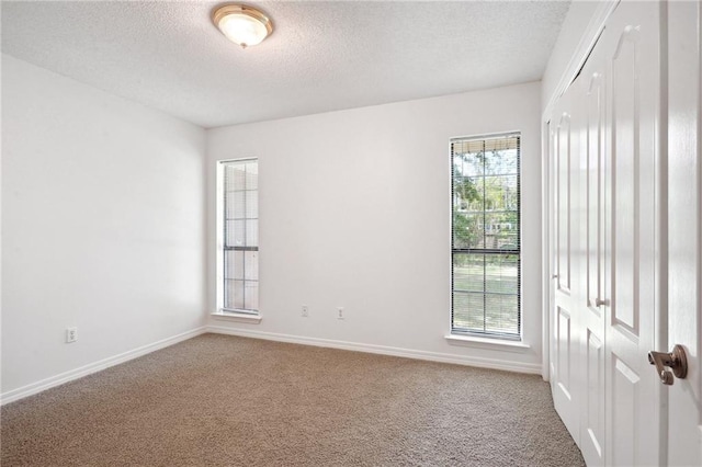 empty room with carpet floors, a textured ceiling, and baseboards
