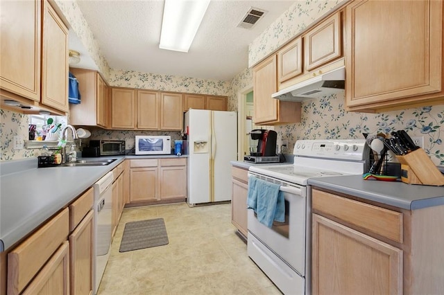 kitchen with white appliances, under cabinet range hood, a sink, wallpapered walls, and light brown cabinetry