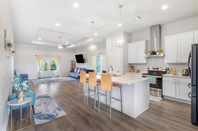 3225 Delaware Ave, Kenner, LA 70065 - kitchen featuring electric range, wall chimney range hood, open floor plan, white cabinetry, and a center island with sink