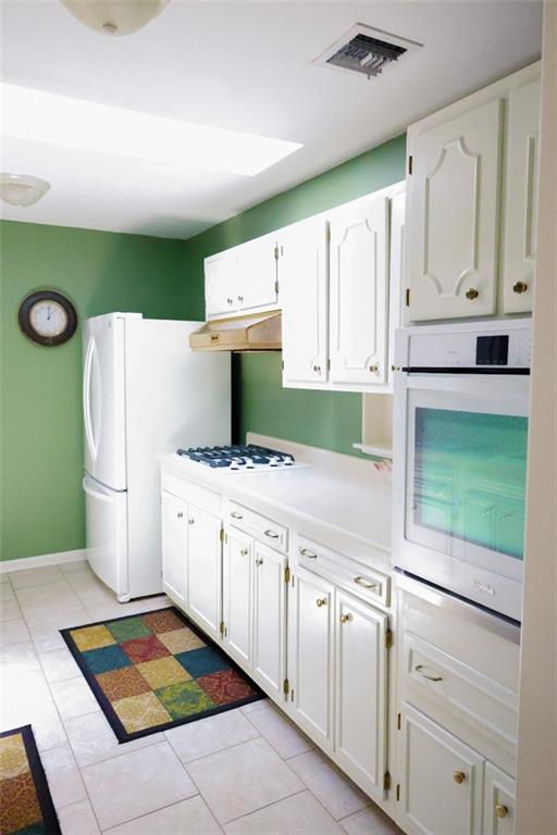 1513 Mason Smith Ave, Metairie, LA 70003 - kitchen featuring white appliances, under cabinet range hood, white cabinets, light countertops, and light tile patterned flooring