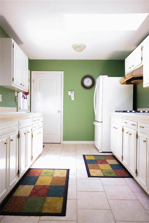 1513 Mason Smith Ave, Metairie, LA 70003 - kitchen featuring under cabinet range hood, white cabinetry, light tile patterned floors, and white appliances