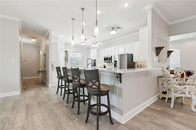 31057 Woodland Dr, Lacombe, LA 70445 - kitchen featuring appliances with stainless steel finishes, a peninsula, a kitchen breakfast bar, ceiling fan, and white cabinetry