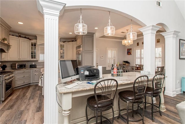 kitchen with decorative columns, high end stainless steel range, dark wood-style floors, a breakfast bar area, and recessed lighting