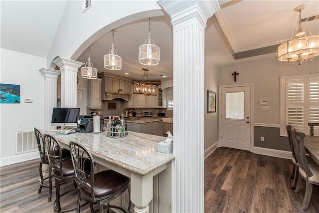 kitchen featuring decorative columns, a chandelier, dark wood-style flooring, light stone counters, and ornamental molding