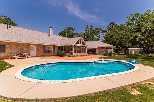 view of pool featuring a sunroom, a patio area, a yard, and an outbuilding