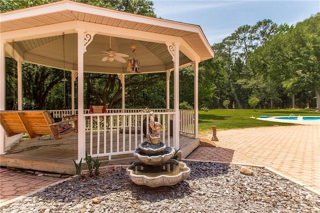 deck with a ceiling fan, a yard, view of wooded area, a gazebo, and an outdoor pool