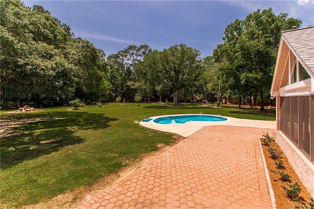 outdoor pool featuring a lawn, a patio area, and view of wooded area