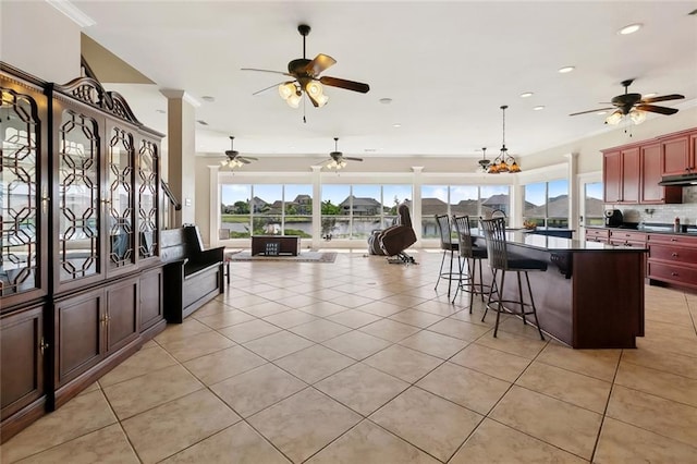 1681 Vela Cv, Slidell, LA 70458 - kitchen with dark countertops, ceiling fan, under cabinet range hood, light tile patterned flooring, and a kitchen bar