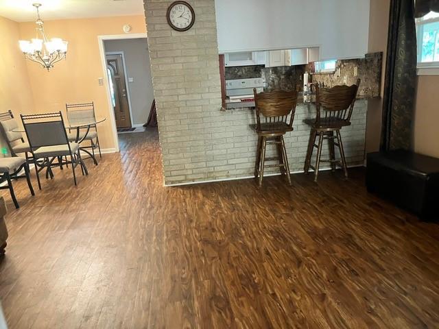 1329 Sigur Ave, Metairie, LA 70005 - kitchen with dark wood-type flooring, white cabinetry, a chandelier, stove, and a kitchen bar