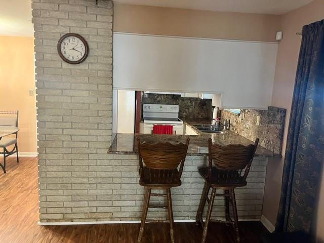 1329 Sigur Ave, Metairie, LA 70005 - kitchen featuring white electric range oven, wood finished floors, a sink, a kitchen breakfast bar, and baseboards