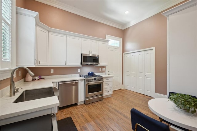 4119 S Liberty St, New Orleans, LA 70115 - kitchen with appliances with stainless steel finishes, a sink, white cabinets, light wood finished floors, and ornamental molding