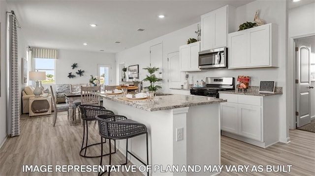 311 Holmes Blvd, Terrytown, LA 70056 - kitchen featuring appliances with stainless steel finishes, light wood finished floors, light stone countertops, white cabinets, and a kitchen bar