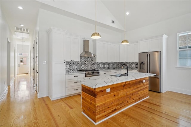 5519 Wingate Dr, New Orleans, LA 70122 - kitchen with high end appliances, wall chimney range hood, white cabinetry, tasteful backsplash, and light wood-style floors