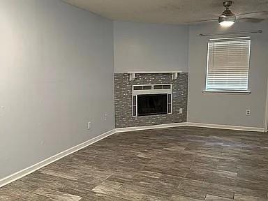 unfurnished living room featuring ceiling fan, wood finished floors, baseboards, and a tiled fireplace