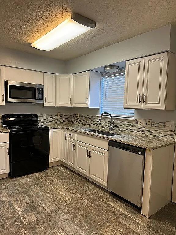 kitchen featuring appliances with stainless steel finishes, white cabinetry, dark wood-style flooring, a sink, and a textured ceiling