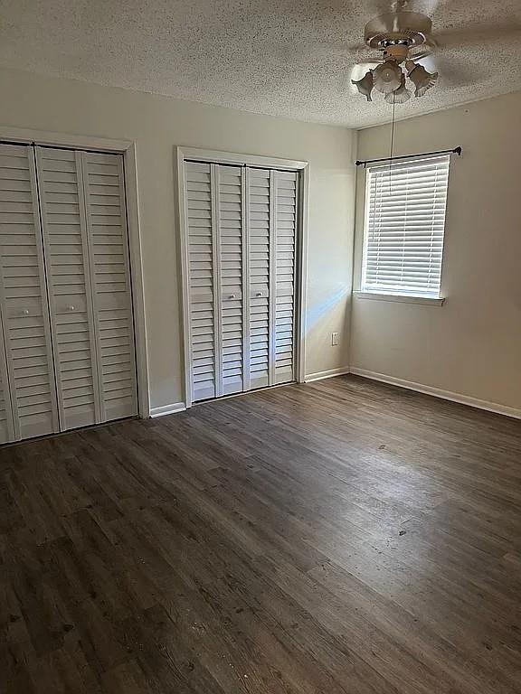 unfurnished bedroom featuring a textured ceiling, dark wood-style flooring, multiple closets, baseboards, and ceiling fan