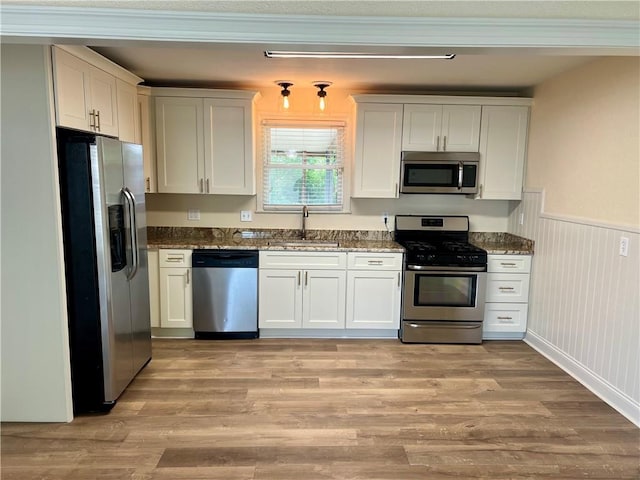 817 N Sibley St, Metairie, LA 70003 - kitchen featuring stainless steel appliances, a sink, dark stone counters, light wood-type flooring, and wainscoting