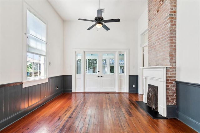 3119 Dauphine St, New Orleans, LA 70117 - unfurnished living room with hardwood / wood-style flooring, a wainscoted wall, ceiling fan, a fireplace with raised hearth, and a high ceiling