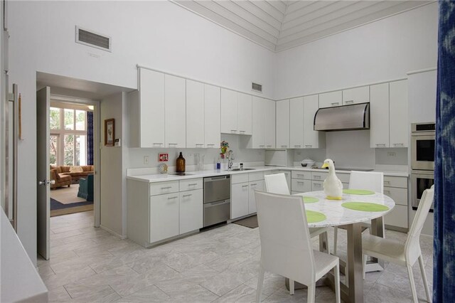 1450 Pine Tree Rd, Opelousas, LA 70570 - kitchen featuring a towering ceiling, under cabinet range hood, stainless steel appliances, light countertops, and white cabinets