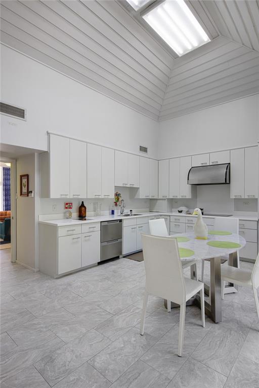 1450 Pine Tree Rd, Opelousas, LA 70570 - kitchen featuring high vaulted ceiling, under cabinet range hood, stainless steel dishwasher, light countertops, and white cabinetry