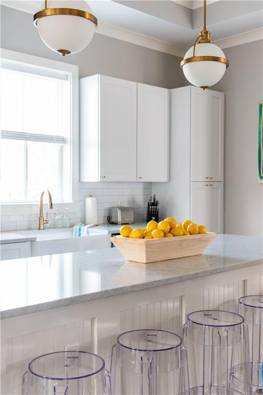 415 N Dupre St, New Orleans, LA 70119 - kitchen with a breakfast bar area, white cabinetry, tasteful backsplash, light stone counters, and hanging light fixtures